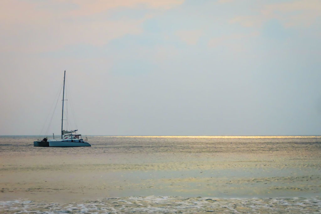 Boat sailing on sea with sun rays on the horizon in the water