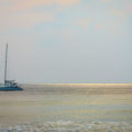 Boat sailing on sea with sun rays on the horizon in the water