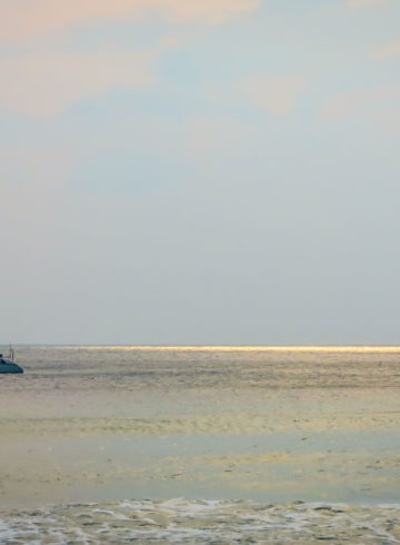 Boat sailing on sea with sun rays on the horizon in the water