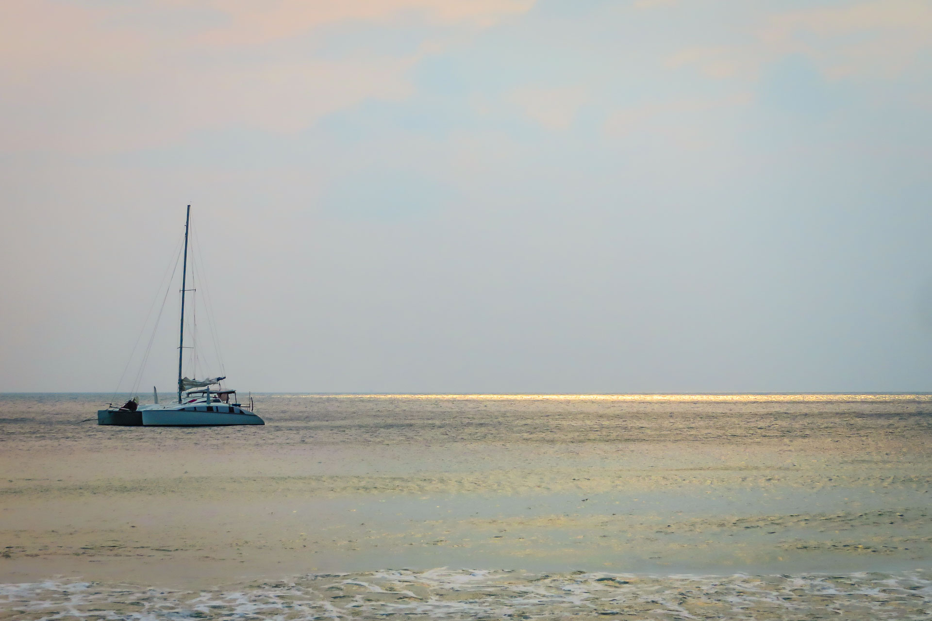 Boat sailing on sea with sun rays on the horizon in the water