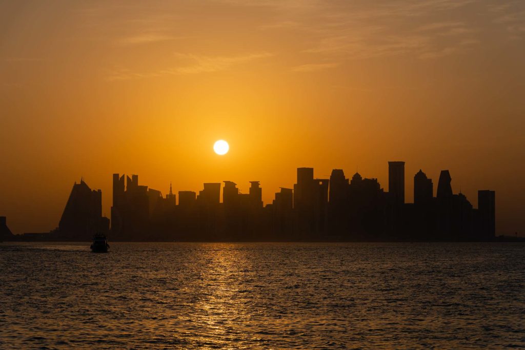 A vista do barco da cidade de Doha com o sol se pondo entre os prédios