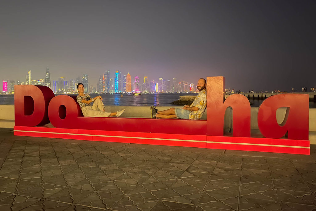 Tiago and Fernanda laying down on a large sign written Doha in the Corniche