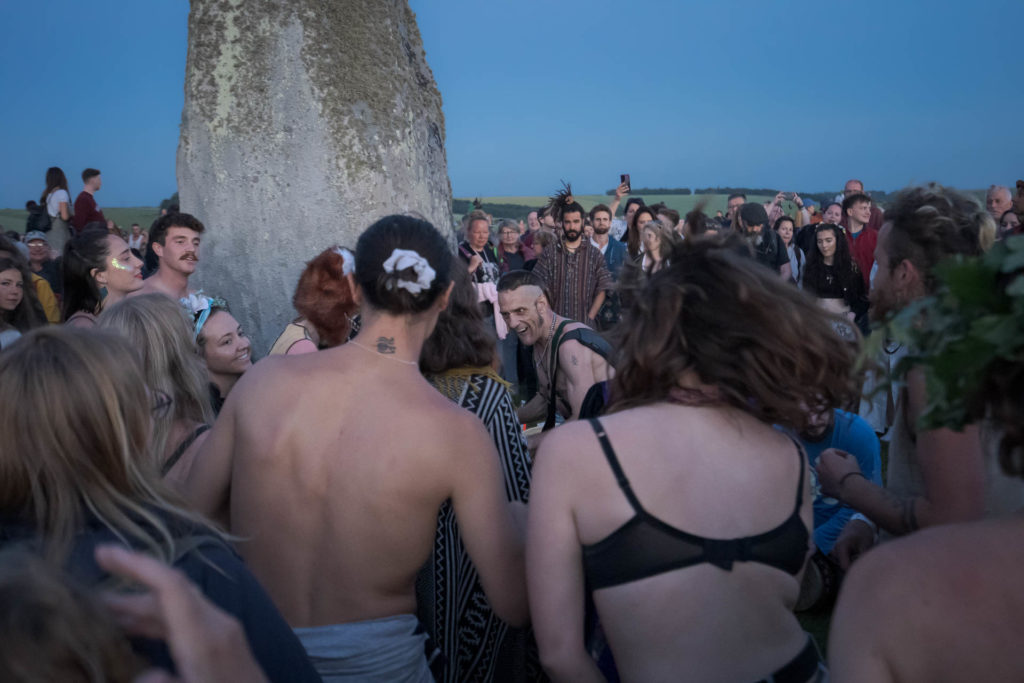 Homem tocando tambor rodeado por pessoas dançando durante o solstício de verão de Stonehenge