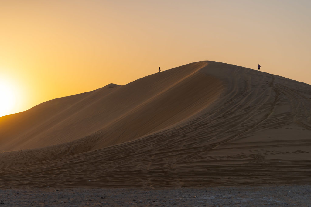 Uma duna gigante com o sol se pondo ao lado no Catar