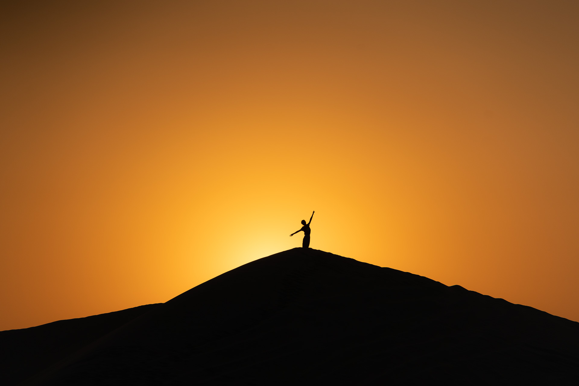 A silhueta da Fernanda no topo de uma duna com o pôr-do-sol ao fundo