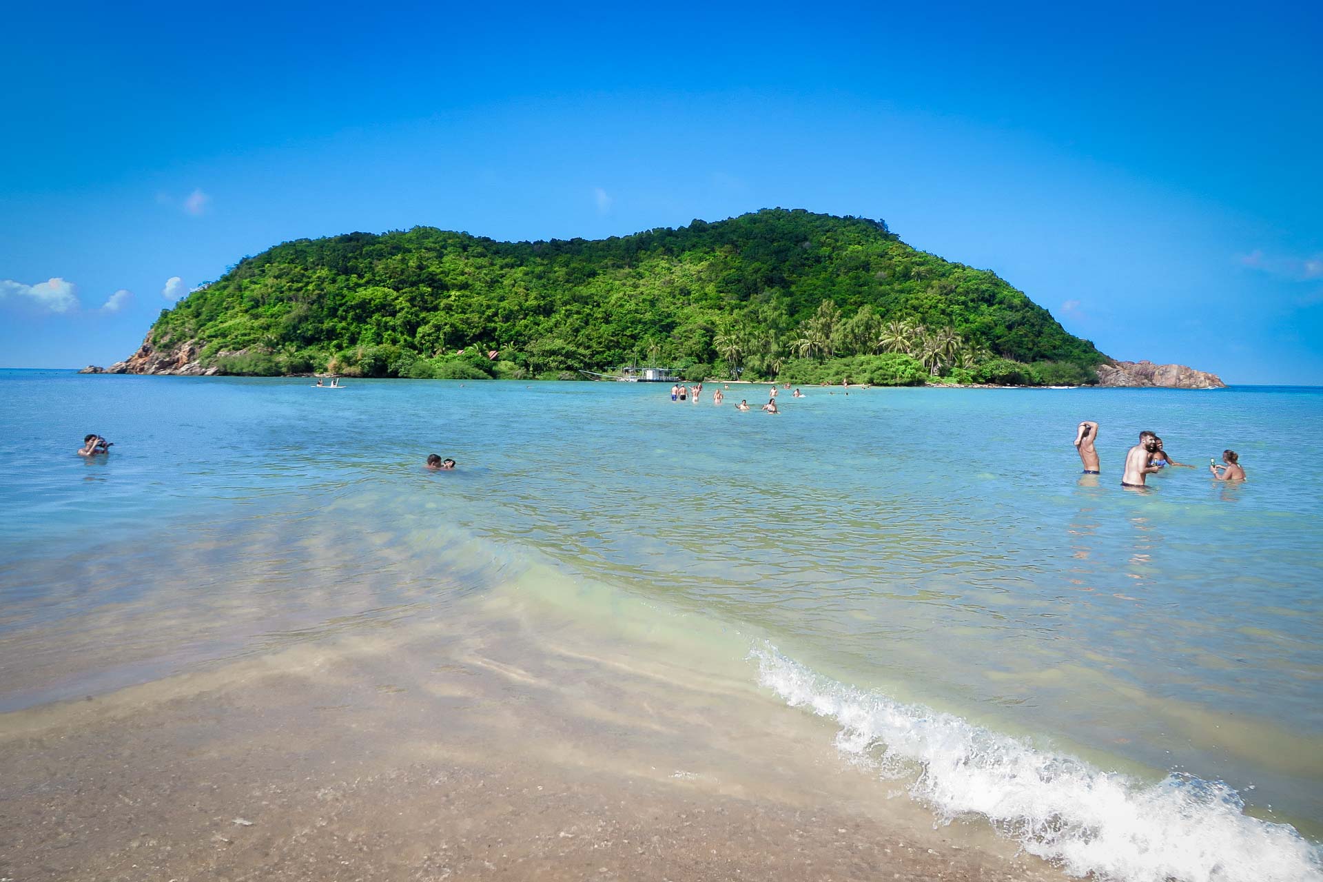 A small island near the beach in the ocean with people swimming around