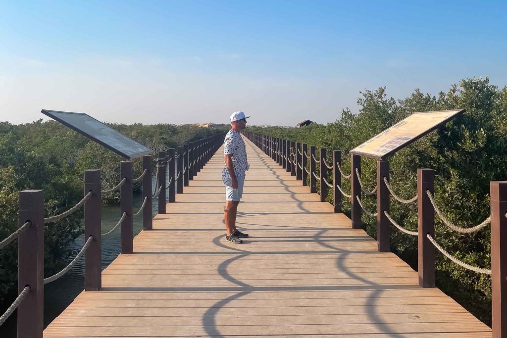 Tiago olhando para a placa de informações na ponte em cima do mangue de Doha