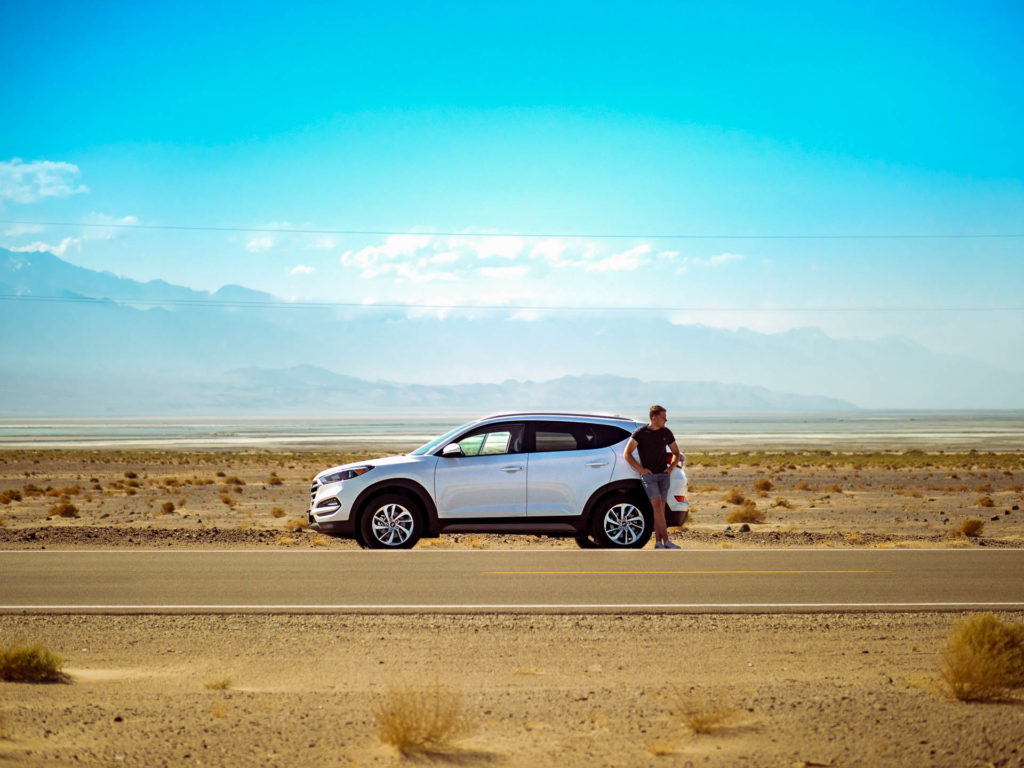 a man with a white car parked in the highway with a large desert behind him