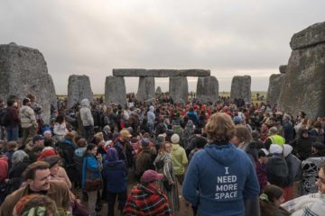 Muitas pessoas no meio das pedras de Stonehenge sendo observada de costas por uma outra pessoa