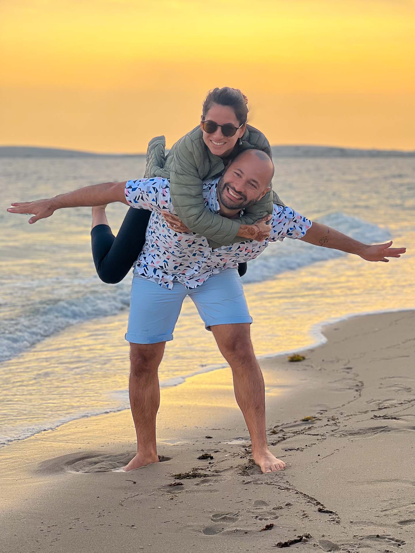 Tiago segurando Fernanda nas costas na praia do Qatar