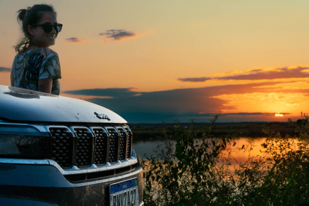 The sunset in Pantanal tour with Fernanda leaning on a car watching the horizon all red from the sunset