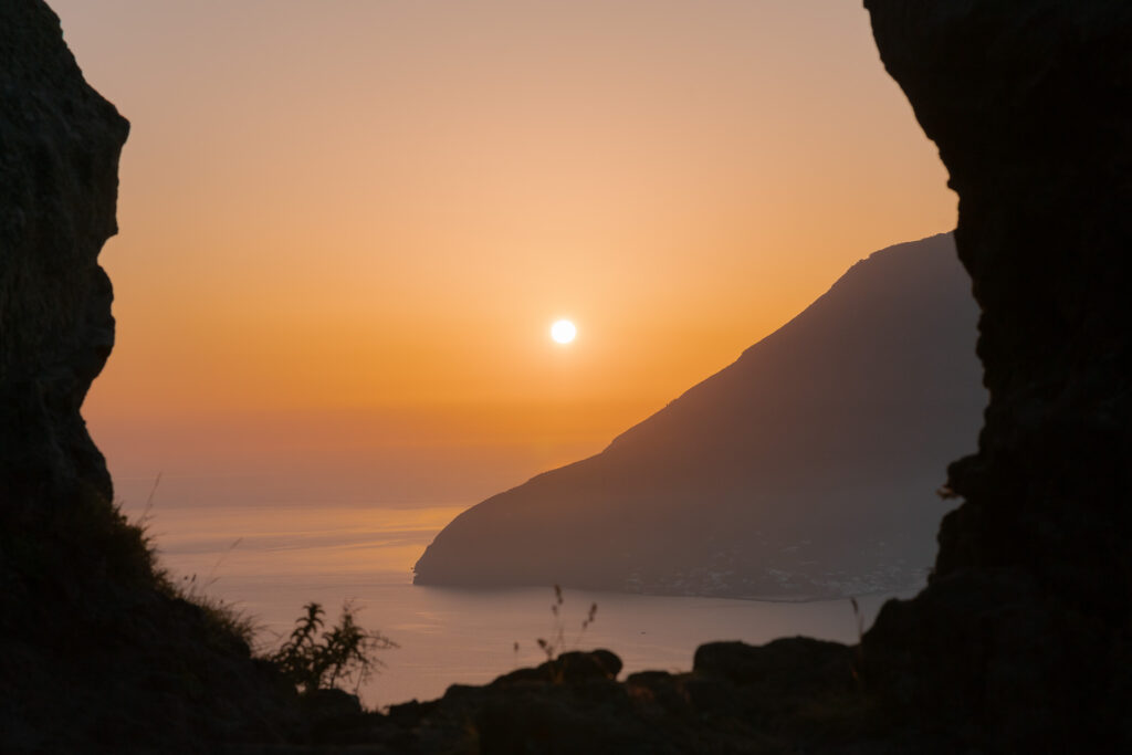 The sunset on the horizon behind the mountain in between two rocks