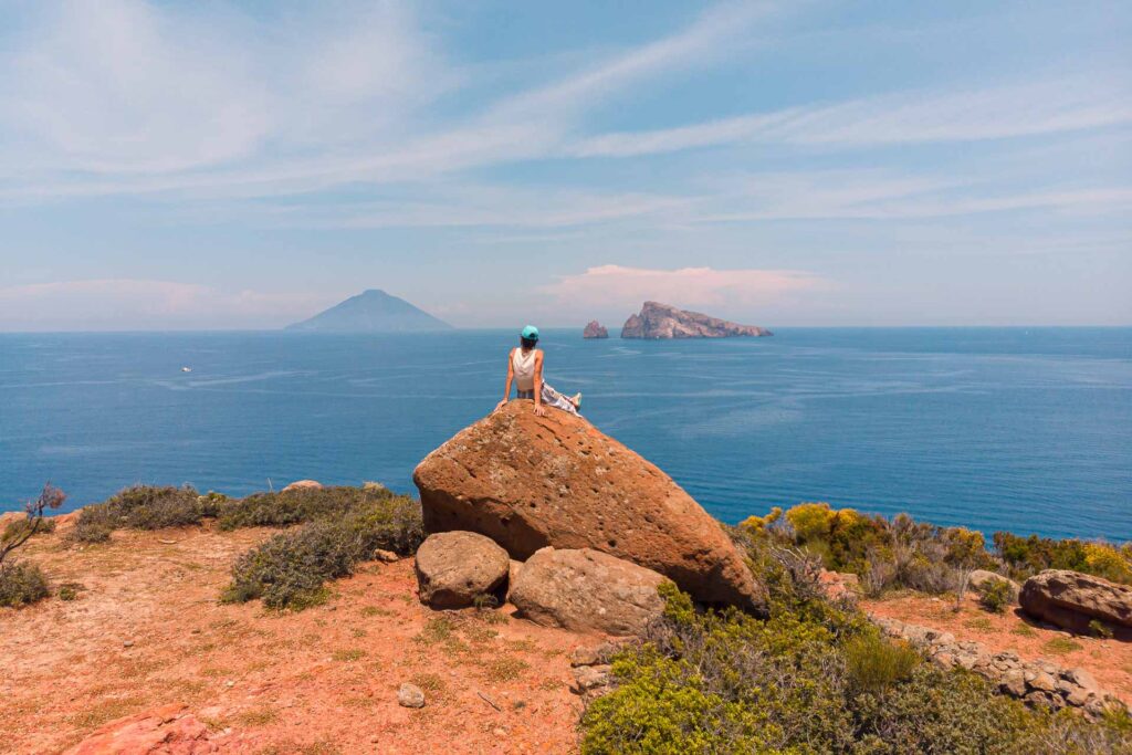 Fernanda sentada numa pedra olhando para o vulcão de Stromboli e para as ilhas de Panarea