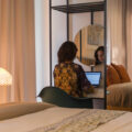Fernanda sentada ao lado da cama na escrivaninha do quarto com seu laptop trabalhando no Hanna Boutique Hotel em Teerã