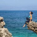Fernanda sentada em cima de uma formação rochosa natural de frente para o mar na Sicília