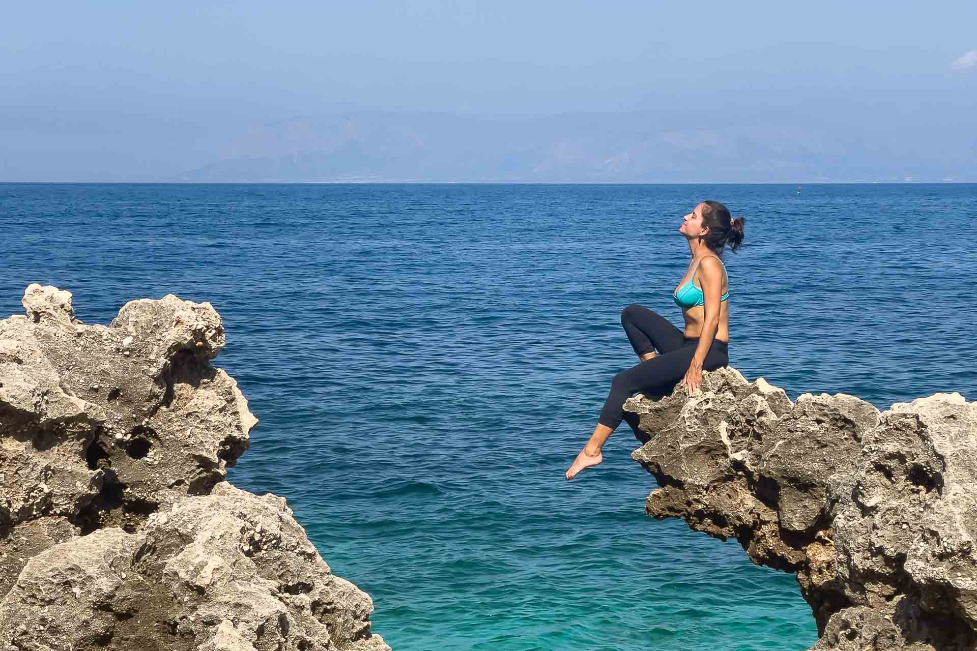 Fernanda sentada em cima de uma formação rochosa natural de frente para o mar na Sicília