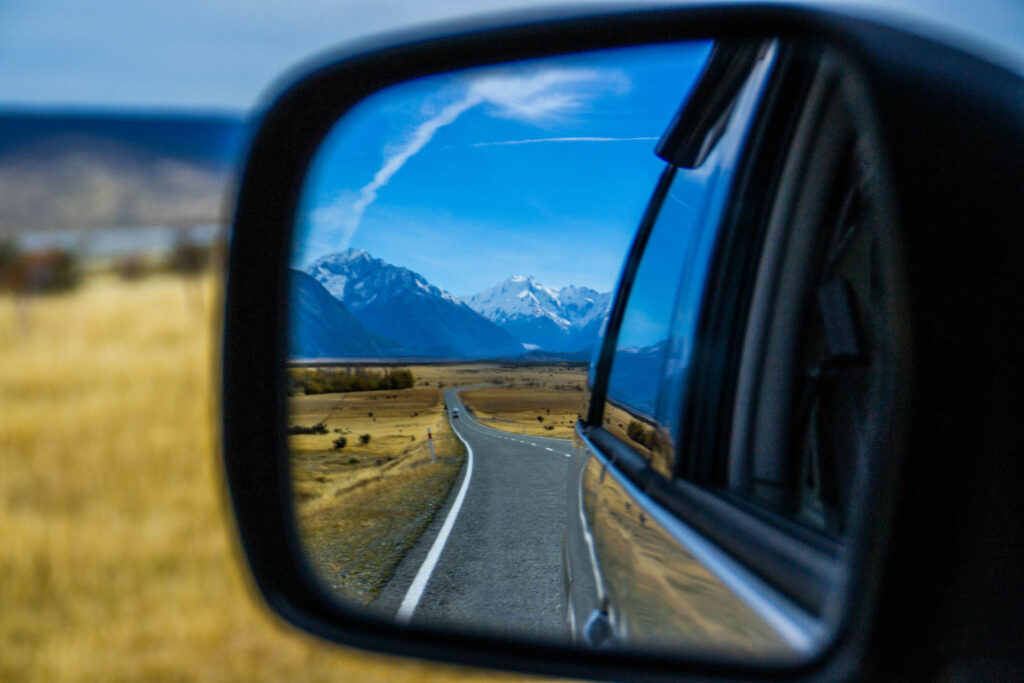 A mirror of a car showing the mountains in the end of the road in New Zealand