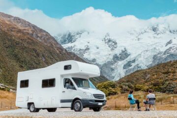 Motorhome camper van RV road trip on New Zealand. Couple on travel vacation adventure. Tourists looking at view of Aoraki Mount Cook National park and mountains next to rental car. Panoramic banner.