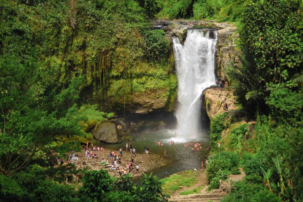 The large Tegenungan waterfall falling in a pool swimming by many people