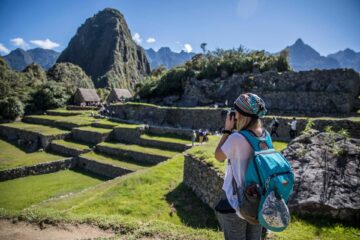Blonde woman with camera taking pictures of machu picchu in a beautiful summer day with a blue sky.