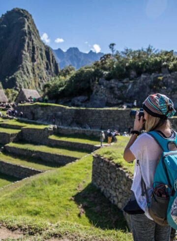 Blonde woman with camera taking pictures of machu picchu in a beautiful summer day with a blue sky.